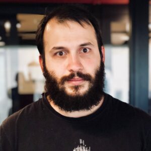 A portrait of myself. I'm wearing a black t-shirt. I have a full, thick, black beard. My hair is short and thin. My eyebrows are small and thinning.