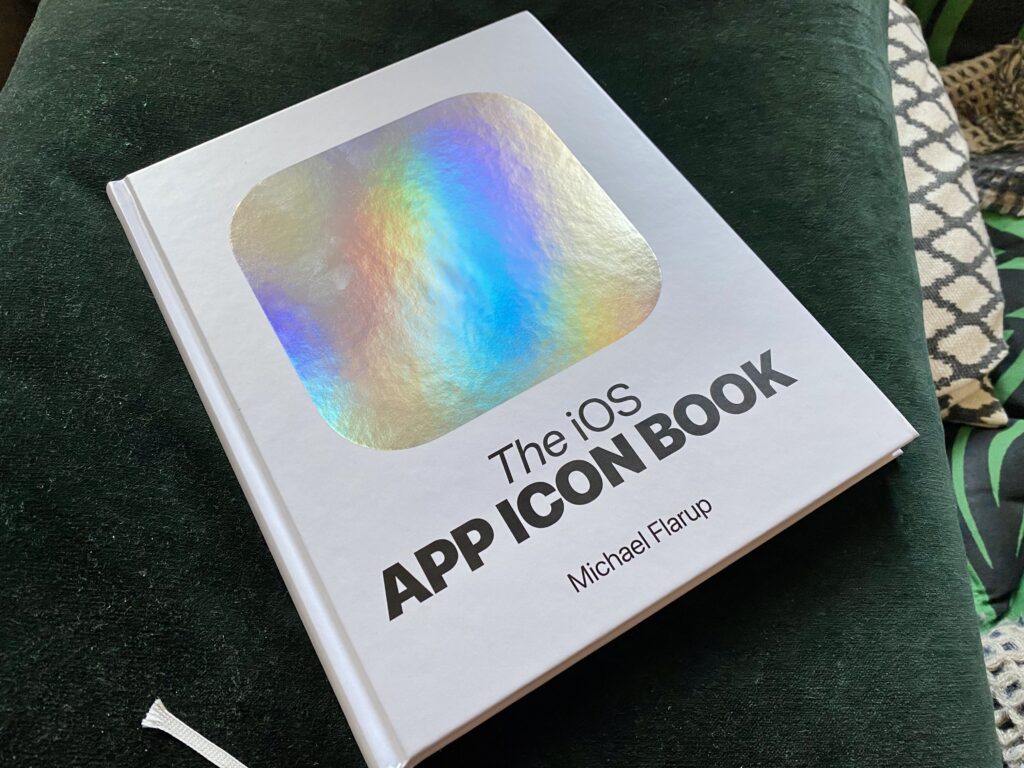Cover of the iOS App Icon Book. The cover features a white background with a big silver reflective rounded square shape on the center